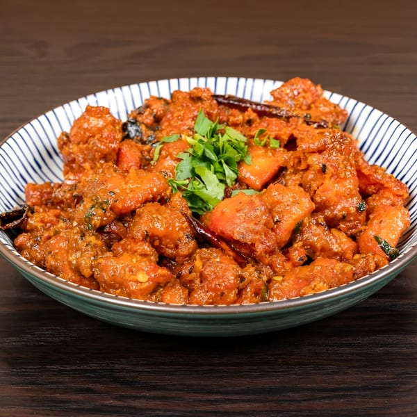 A close-up of a bowl of Indian chicken curry, garnished with fresh cilantro, on a dark wooden table.