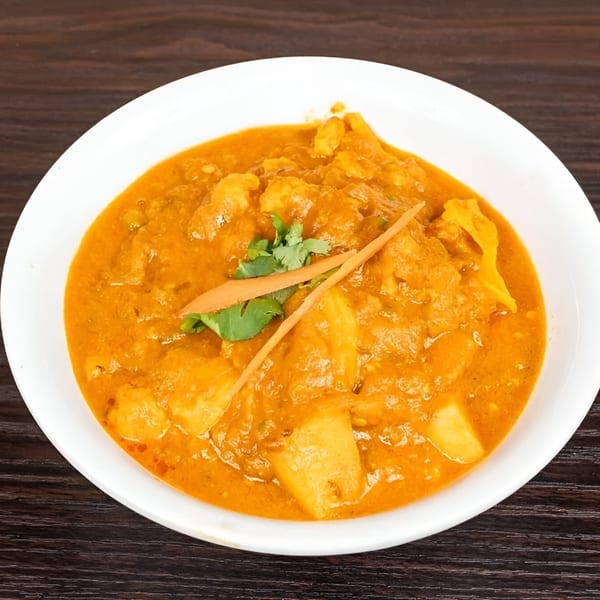 A white bowl filled with orange Indian curry, garnished with cilantro and carrot strips.