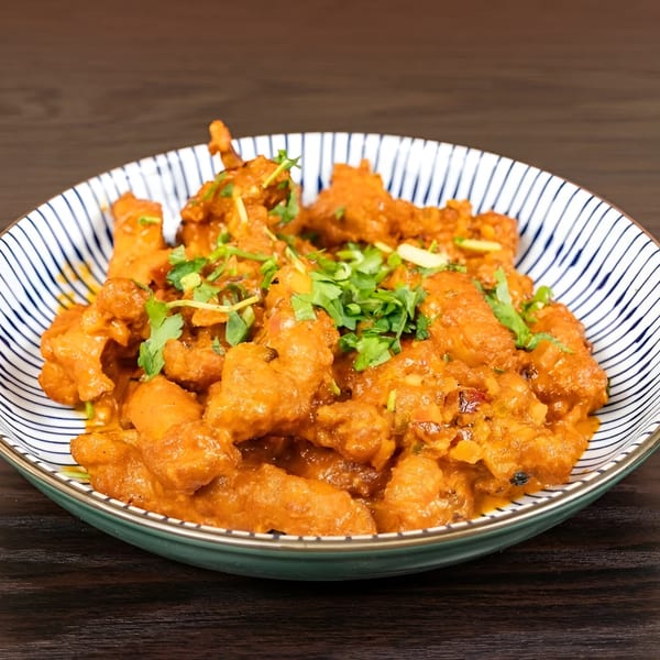 Indian chicken 65, a spicy fried chicken dish, garnished with fresh cilantro in a striped bowl.