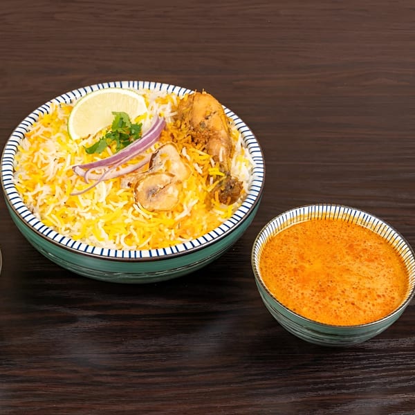 Chicken Biryani from Biryani Pot, garnished with lime, cilantro, and red onion, with a side of curry.
