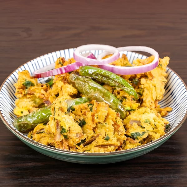 A bowl of golden-fried Indian pakora, garnished with green chilies and red onion rings.